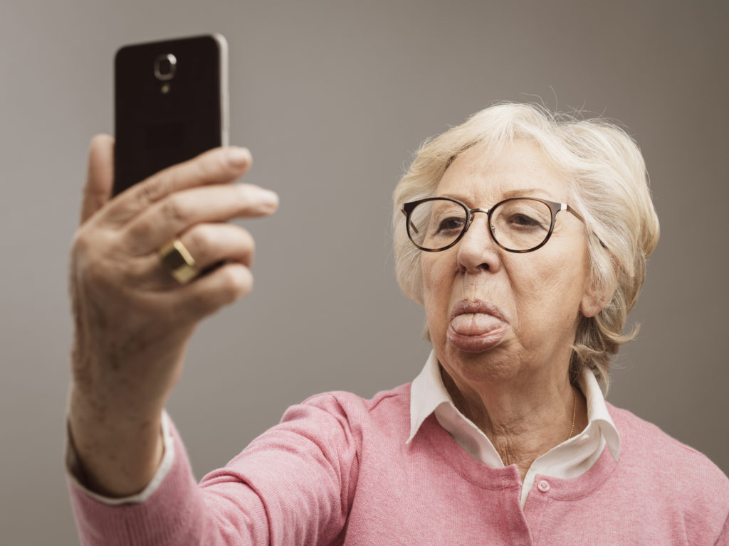 Funny senior lady taking selfies with tongue out using her smartphone